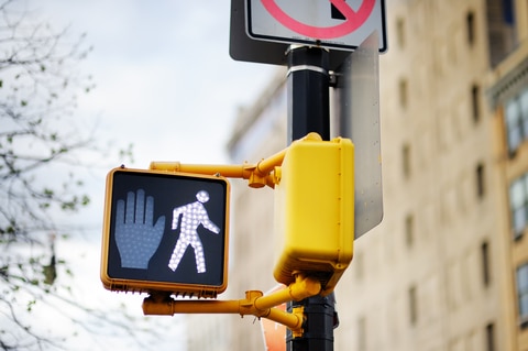 Illuminated pedestrian crosswalk sign showing a walking person symbol.